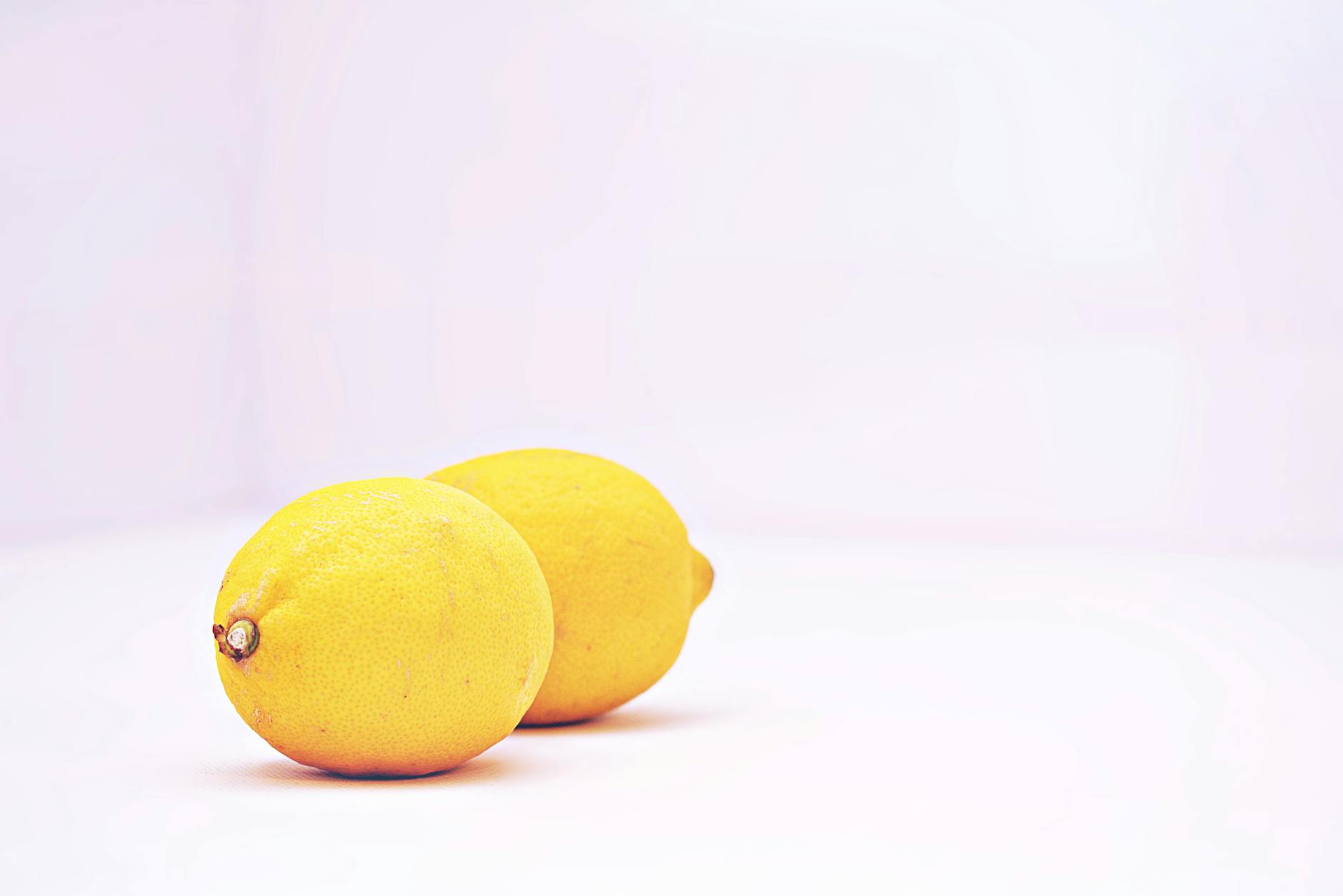 A hand holding a fresh lemon on soft pink background, representing sensitive postpartum healing