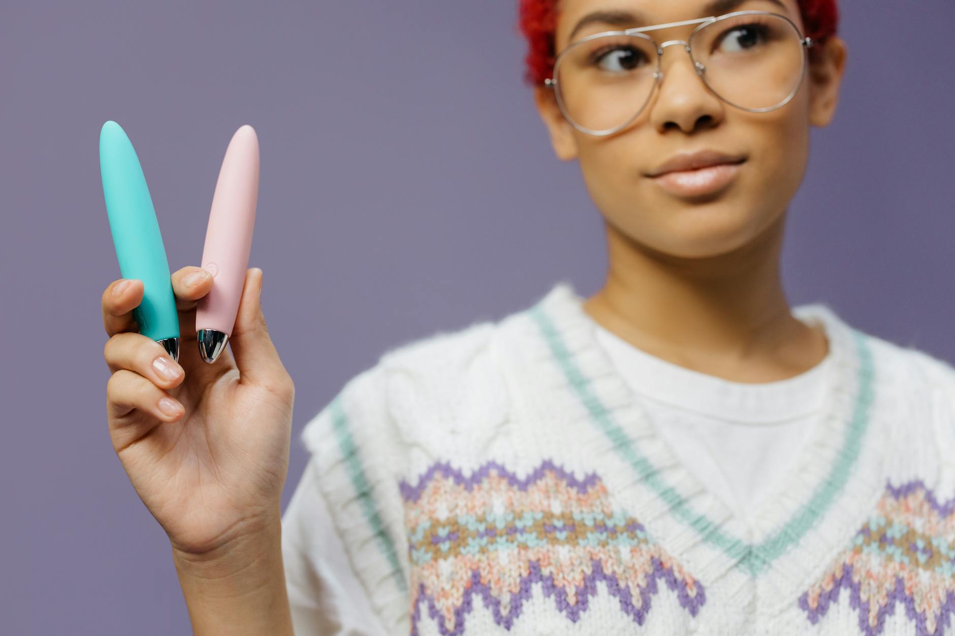 A woman holding a colorful vibrator against a purple background, representing pleasure and self-care