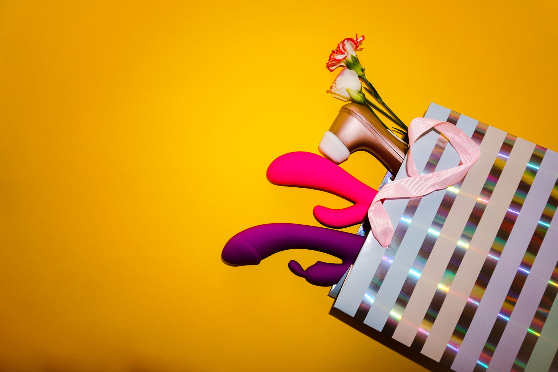 Vibrators with flowers in a holographic gift bag against a bold yellow background