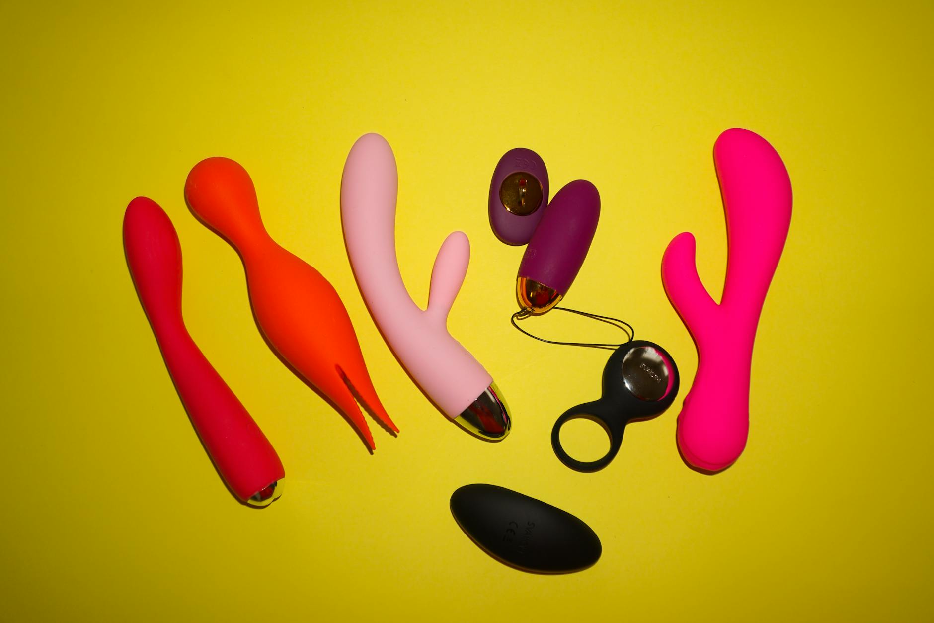 Colorful clitoral vibrators and sex toys arranged on a bright yellow background, including the Lem by Hellanancylemon